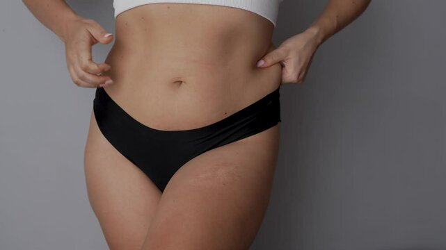 Fat deposits on the abdomen. Young woman grabbing for belly and sides fat on a dark grey background. Overeating, overweight, excess weight, hormonal belly, swelling of the body