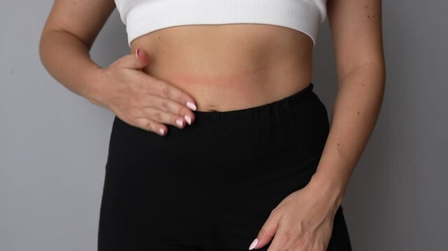 Young woman stroking her belly in a circle with her hand to speed up the digestion of food on a grey background. Health care, good digestion. The girl shows a feeling of hunger. Overeating