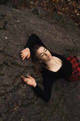 a woman lies on her back on a large stone in the forest.  Her arms are extended upward, her eyes are closed, her face is turned upward.