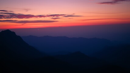 Obraz premium Serene sunset over silhouetted mountain ranges, painting the sky with vibrant hues of pink and orange, a breathtaking natural landscape.