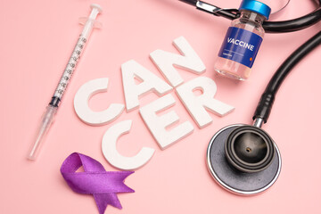 A vaccine syringe stethoscope and purple ribbon lie near the word CANCER. World cancer day concept background