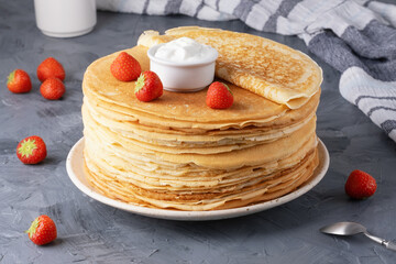 Pancakes with sour cream and strawberries on a grey table.