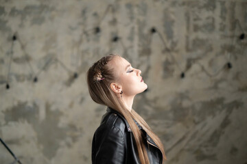 A woman showcasing a distinctive haircut stands tall with her eyes closed, expressing confidence in an artistic background