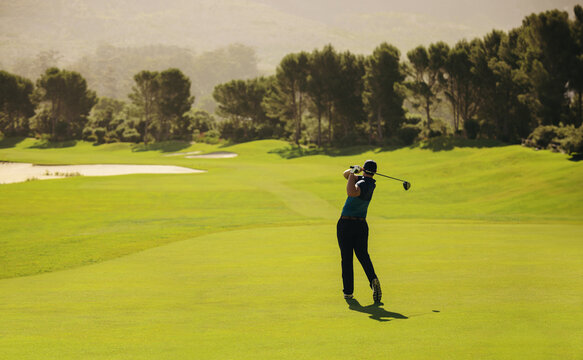 Golfer swinging with precision and follow through on a vibrant golf course fairway shot during a sunny day