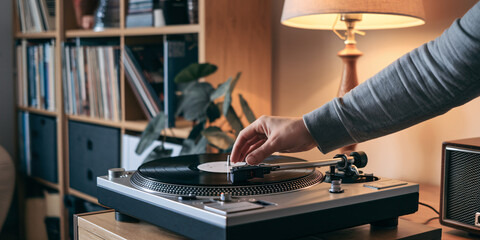 Vinyl Record Being Placed on Turntable. A close-up captures a hand gently placing a vinyl record onto a turntable in a warmly lit home setting.