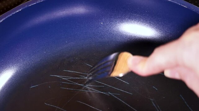 Fork scratching the nonstick coating on a frying pan