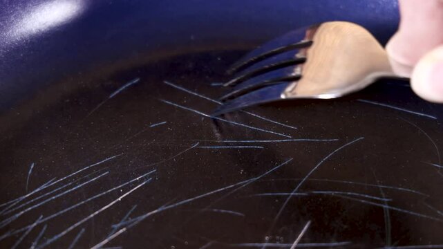 Close up of a fork scratching the non stick coating on a frying pan