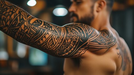 Close-up of a man's muscular arm with intricate tribal tattoos in an indoor setting with blurred background and soft lighting Copy Space