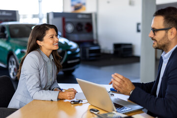 Smiling happy female manager car salesman in car dealership signing contract at table with male buyer in suit