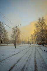 Winter city with snowy weather cold on the picture,snowy landscape .Road and trees , beautiful sunrise over the sunrise , branches and buildings on street.