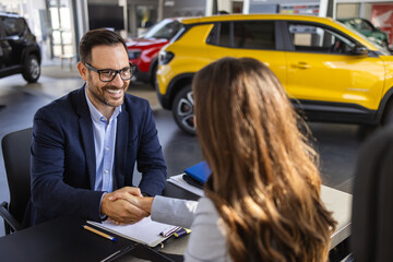 Young woman signing car insurance document or lease paper contract or agreement. Beautiful woman Buying New Car Signing Papers With Dealer Man Standing In Auto Dealership Store.