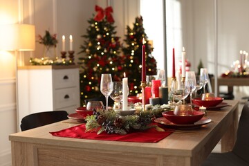 Christmas table setting with stylish dishware, glasses and burning candles in festive decorated room