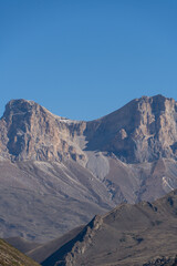 Kabardino-Balkaria. El-Tyubu. Rocky mountains with trees growing on their slopes glow in morning sun. Close-up. Chegem Gorge. Unique rocky ridge with steep cliffs against blue autumn sky.