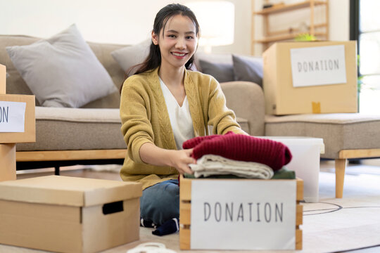 Smiling woman folding clothes for donation, organizing items in a cozy living room with donation boxes