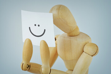 Sad Wooden mannequin hides his pain behind a sheet with a drawn smile - Concept of depression and sadness