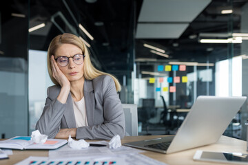 Tired and disappointed businesswoman sitting near documents and scraps of paper. Unsatisfied with...