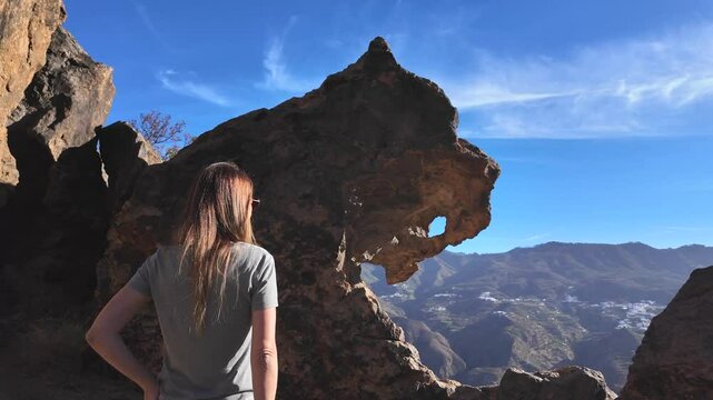 Woman with her back turned admires the rock formation Dog of Bentayga on the island of Gran Canaria, Canary Islands, Spain.
