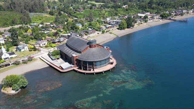 view of Teatro del Lago on blue waters and forested beach with lots of houses in Frutillar, Chile