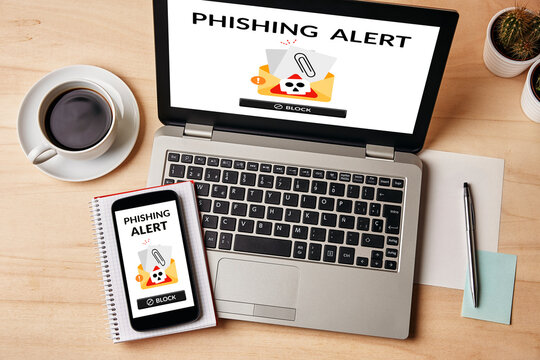 Top view of a phishing alert displayed on both laptop and smartphone screens, placed wooden table. A warning of digital scams in everyday technology.