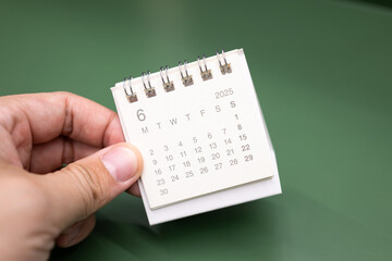 Fototapeta premium Hand holding mini calendar for 2025 JUNE background. Calendar concept with 2025 JUN calendar.