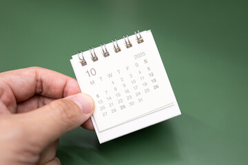 Fototapeta premium Hand holding mini calendar for 2025 OCTOBER background. Calendar concept with 2025 OCT calendar.