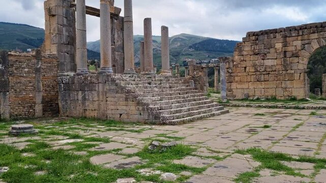 Revealing shot of antique Roman ruins in the historical city of Djemila showing temple entrance gate, columns and stairs on an overcast day