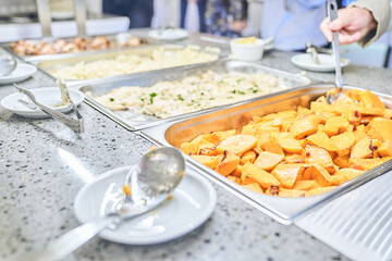 Close-up of a metal container with baked hearty food. A woman puts food in a cup on a buffet table in a restaurant. With space to copy. High quality photo