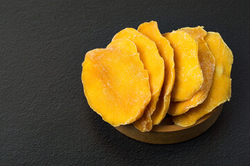 Candied mango in a wooden bowl on a dark background.