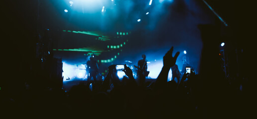 Hand with a phone records live music festival. Audience crowd of people use smart phones enjoying...
