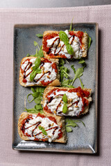 Bruschetta with peppers, cheese, and pine nuts served on a plate, top view