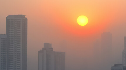 Fototapeta premium hazy sunset over city skyline, with tall buildings silhouetted against orange sun. atmosphere is serene and tranquil