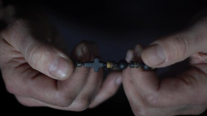 Man's hand holds a wooden rosary with a christian cross. Fingers run over the beads of the rosary during prayer
