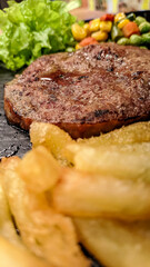 Close up photo of sirloin steak served with vegetables and potatoes on a black platter