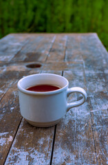 Photo of tea in a white cup, placed on an old wooden table with a natural background around it