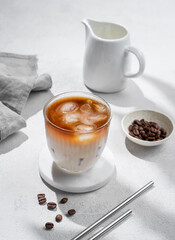 Iced coffee latte in a glass with milk on a light background with coffee beans