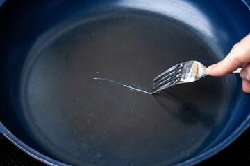 Fork scratching the non stick coating on a frying pan
