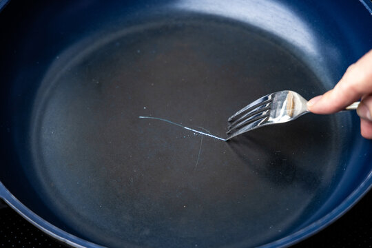 Fork scratching the non stick coating on a frying pan