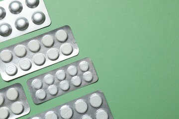 Pills in blister packs on green background, close up