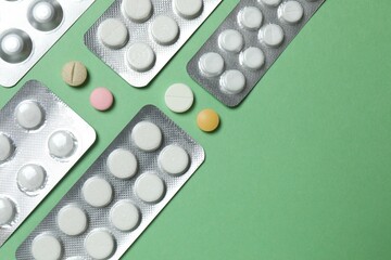 Pills in blister packs on green background, close up