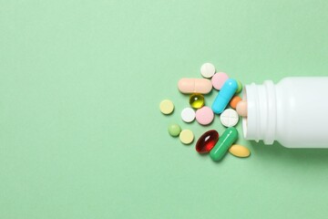 Various pills pouring out of medicine bottle on color background