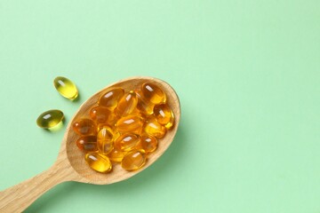 Capsule of omega 3, 6, 9 fish oil, vitamin, food supplement in wooden spoon on color background