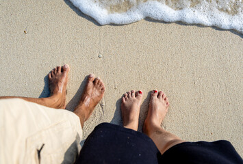 married couple feet with receding sea waves on white sand beach at morning