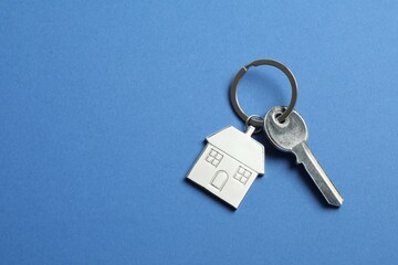 Metallic key with keychain in shape of house on color background