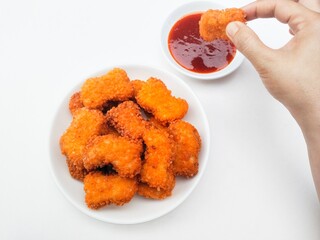Fried chicken nuggets in a white plate and a hand is dipping fried chicken nuggets in sauce in a...
