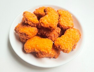 High angle view of fried chicken nuggets in a white plate on a white background. 