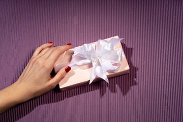 Female hands holding a gift box on a bright background. Gift for Christmas, Valentine's Day, birthday. Beautiful festive background.