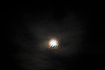 Bright full moon illuminating a cloudy night sky over a tranquil landscape