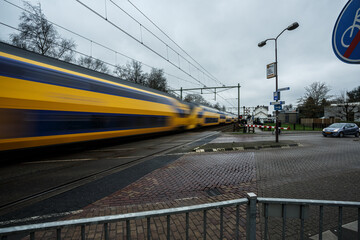 Fototapeta premium Fast train passing through a level crossing in a suburban area during cloudy weather