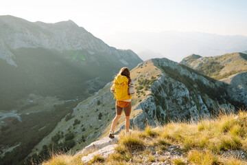 Naklejka premium Woman tourist traveler walking on the top of mountain in summer sunny day under sun light. Beautiful mountains landscape view. Adventure active