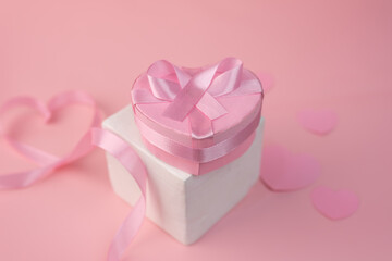 A pink heart shaped gift box sits atop a white square box tied with pink ribbon
